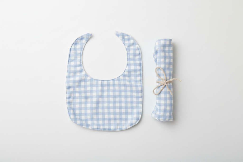 Professional flat lay of light blue gingham bib and rolled burp cloth set