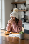 White NBPT beanie woman at kitchen table with coffee and pink sweater